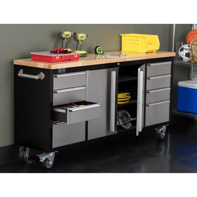 Trinity TLS-7205 (72x19) Black & Stainless Steel Rolling Workbench with some of the drawers opened. Placed against a wall with tools displayed on the worktop.