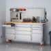 Trinity TLSF-7210 (72x19) PRO Stainless Steel Rolling Workbench w/ Pegboard. Has building/Construction Tools on the Worktop and Pegboard. Top left drawer with Wood Worktop is Opened. Placed next to a wall.